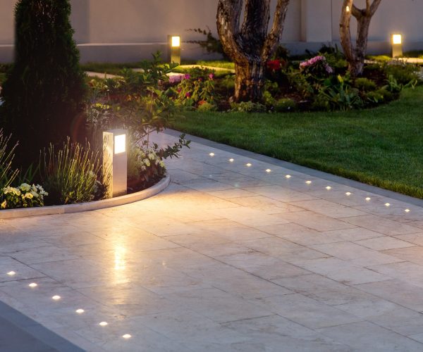 marble tile playground in the night backyard of mansion with flowerbeds and lawn with ground lamp and lighting in the warm light at dusk in the evening.