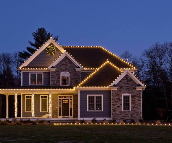 brick and gray home with yellow holiday lights and wreath