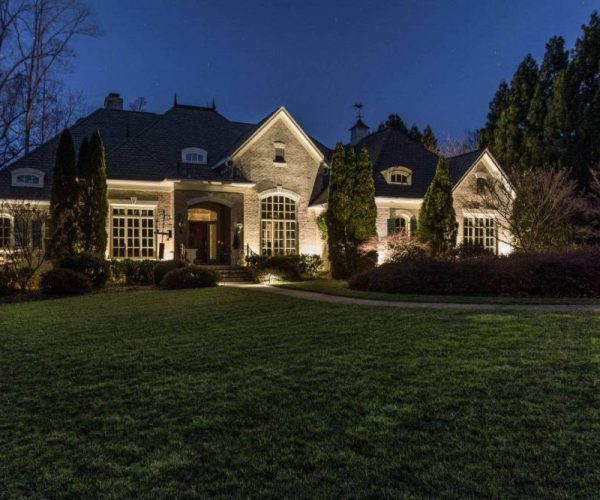 brick home with landscape lighting and trees
